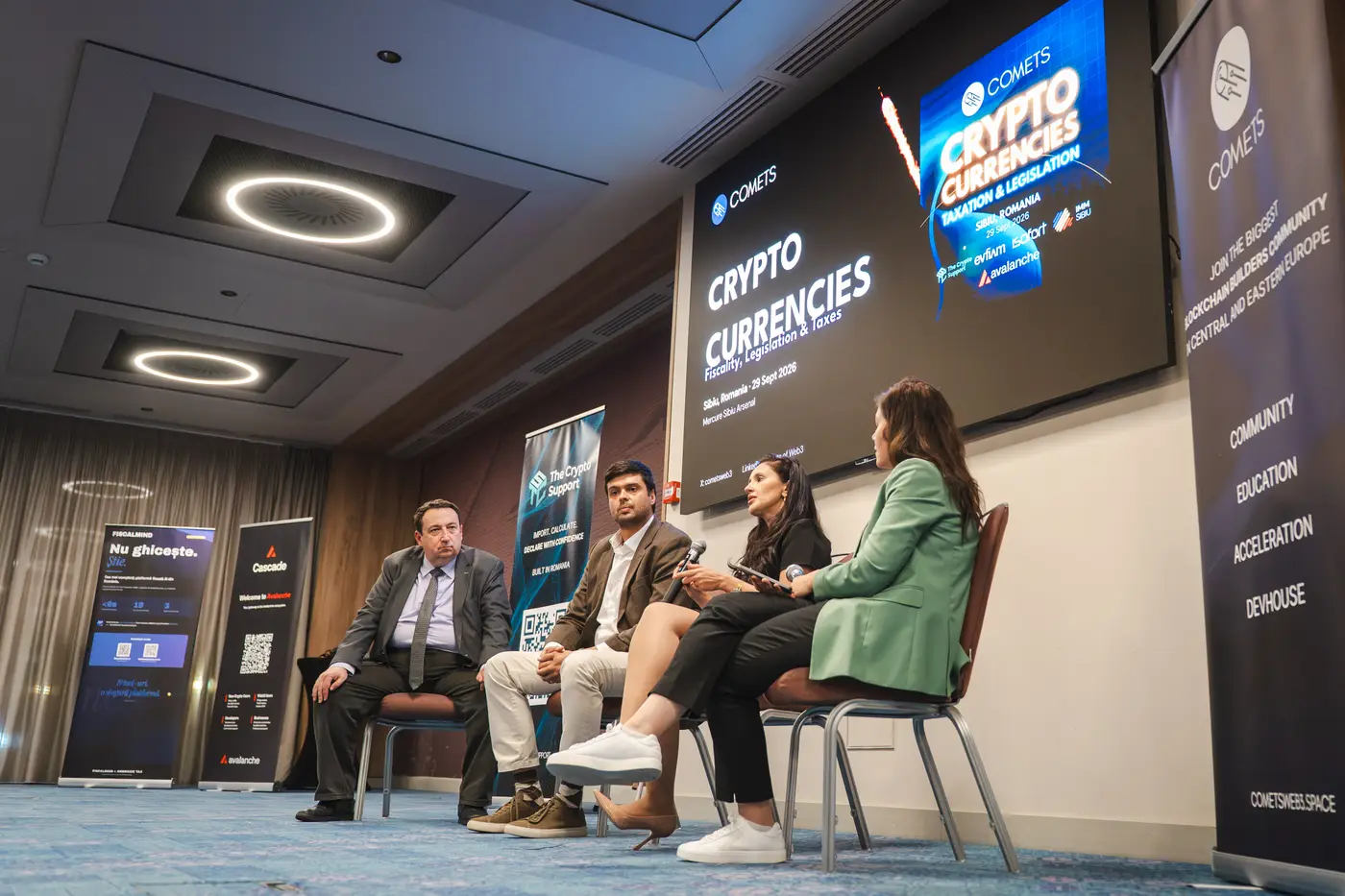 Patru paneliști pe scenă, sub ecranul cu numele evenimentului și logourile partenerilor.