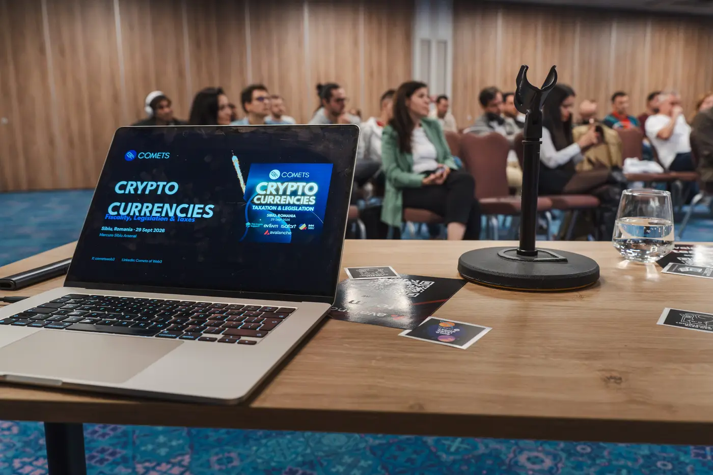 Publicul din sală, văzut de pe masa vorbitorilor, lângă un laptop care afișează prezentarea COMETS.